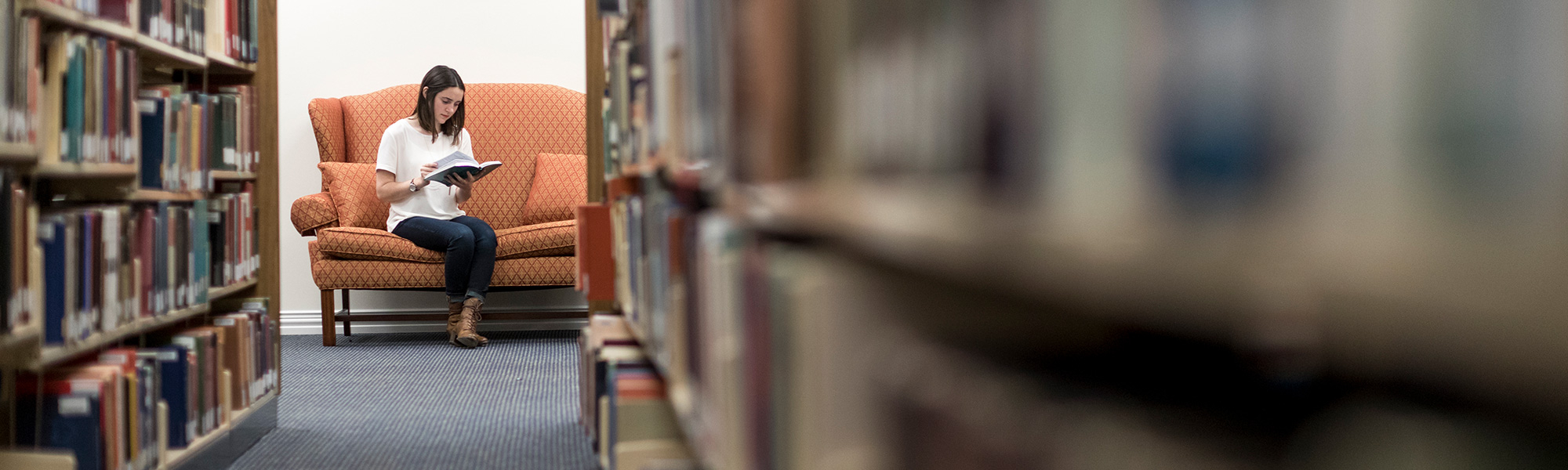 a girl sits on a couch reading in a library