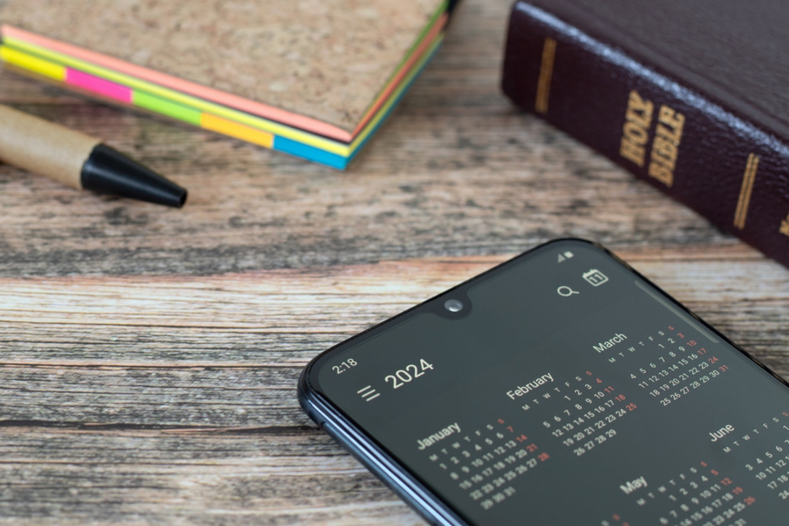 iPhone on wood table with app open and Bible and paper in the background of the table