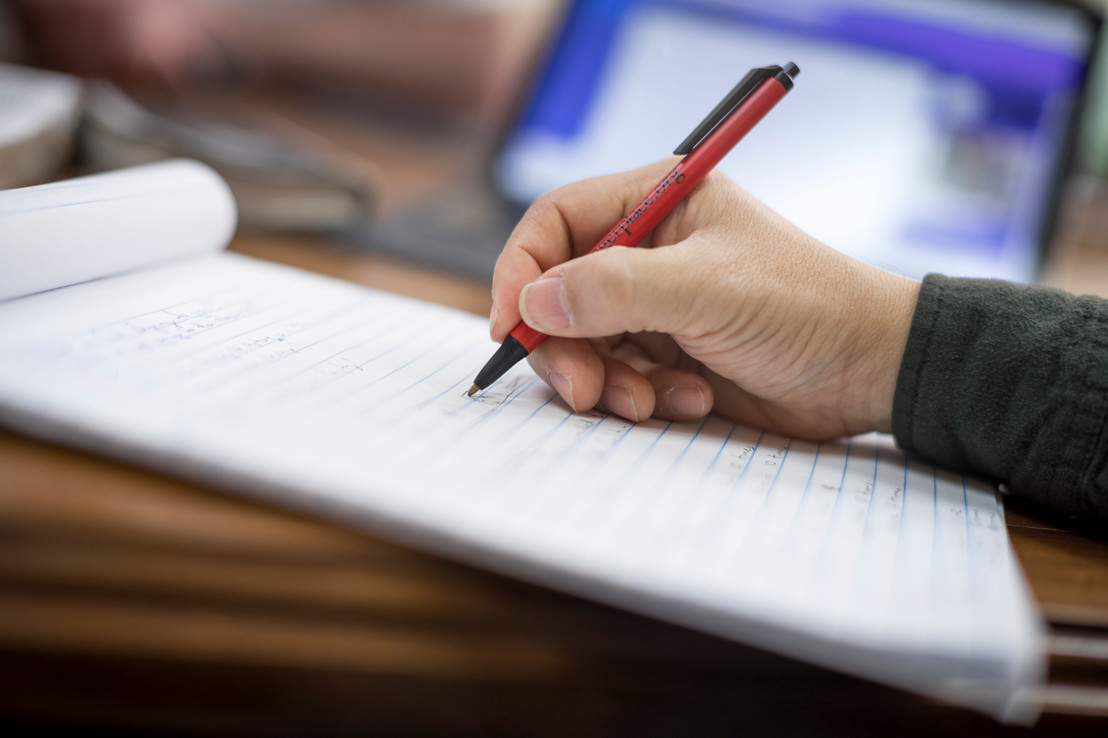 A person holding a red pen writing on a white notepad in Dallas, Texas