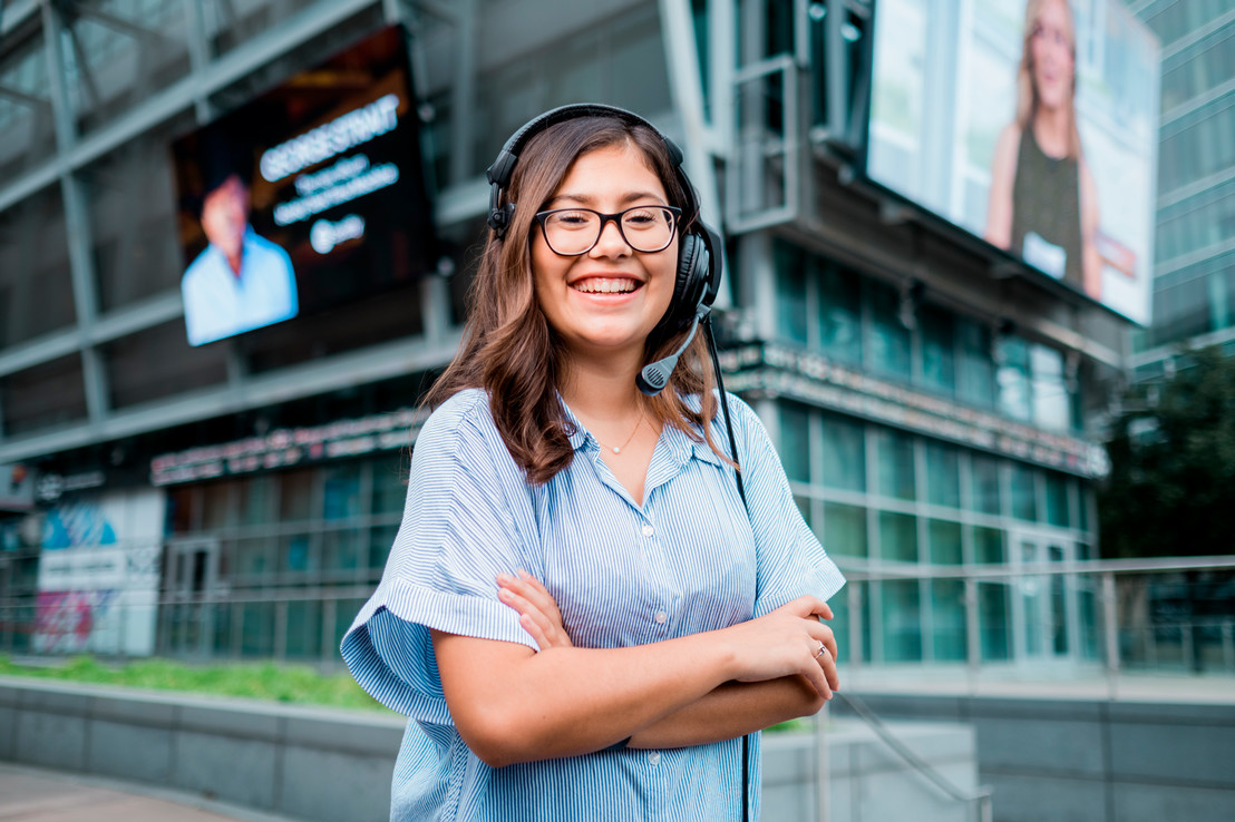 College student standing in Downtown Dallas at Victory Park with giant screens behind her