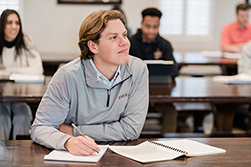 man taking notes in a classroom with students in the background