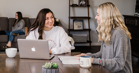 two students sitting at a table smling at each other