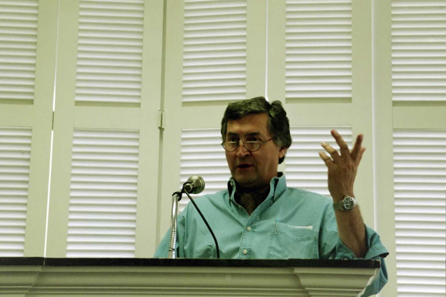 picture of Paul Marshall speaking in front of a podium with one hand raised up in the air