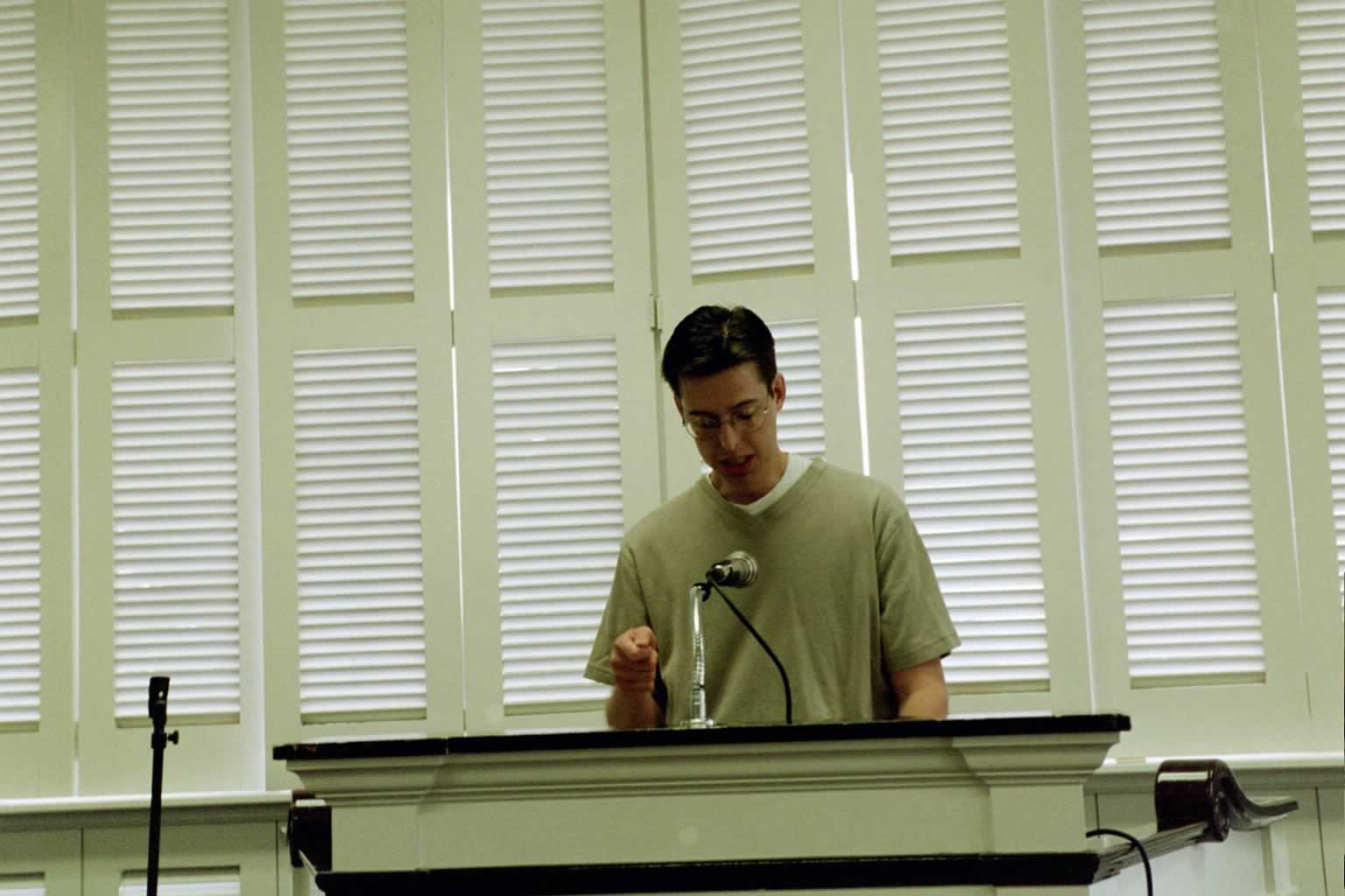 picture of man with glasses reading behind a podium