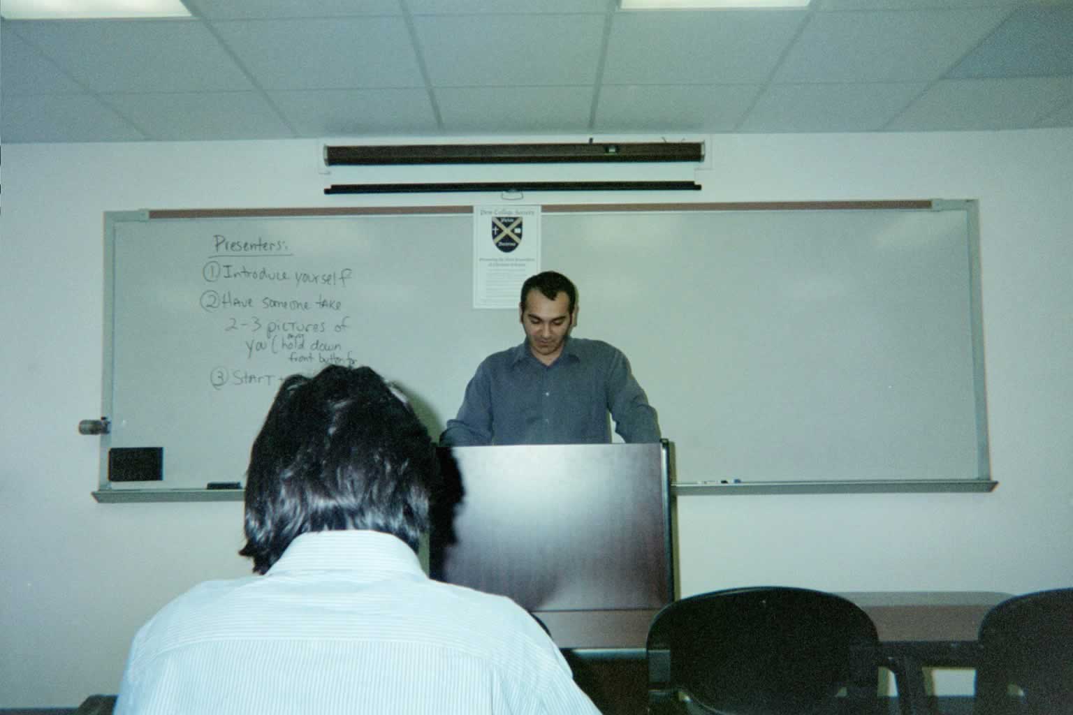 picture of a man standing behind the podium with the back of another man's head in the bottom