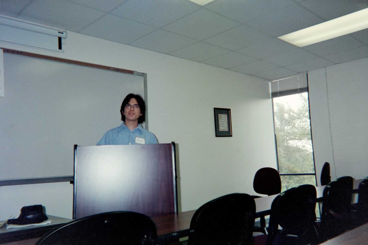 picture of a man in glasses standing behind a podium looking up and speaking