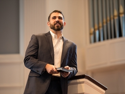 A man stands in front of the podium in the chapel holding a Bible