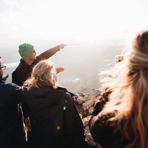 4. A group of people facing away, a man pointing out to the distance (he’s wearing a green hat)