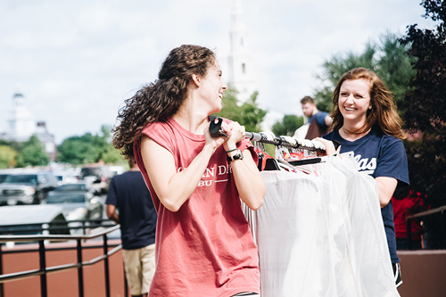 Two girls carrying white shirts on a coat rack outside of Crowley