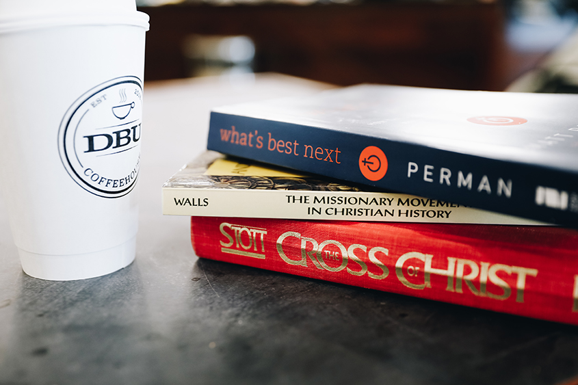 Books stacked on a table next to DBU Coffeehouse coffee