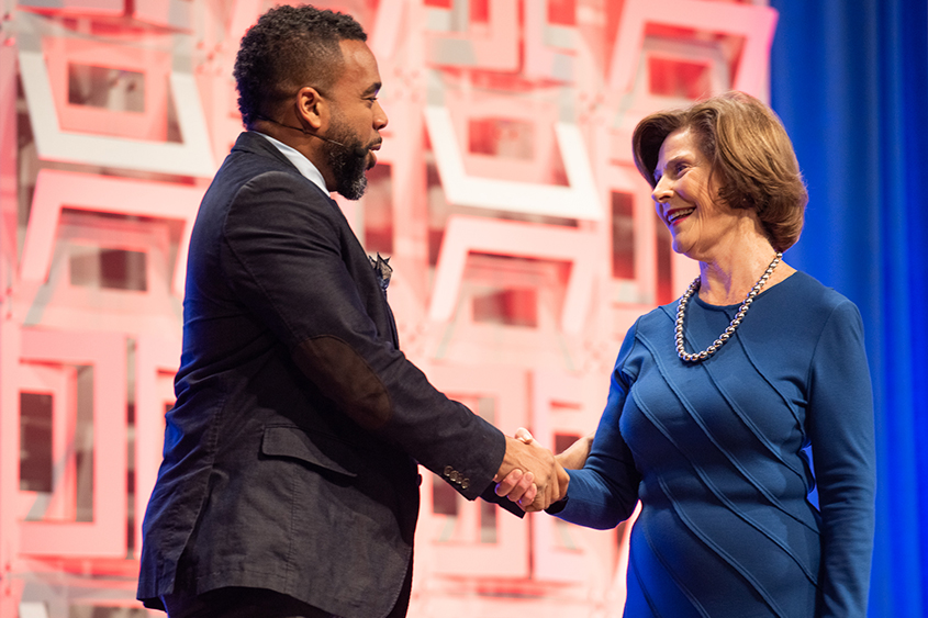 An African American is shaking hands with Barbara Bush on a stage.