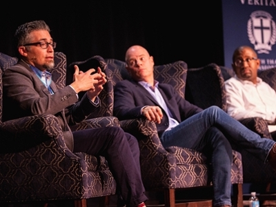 Three men are sitting in chairs on stage. 