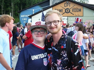 A man is standing with a special needs student. Both are smiling.