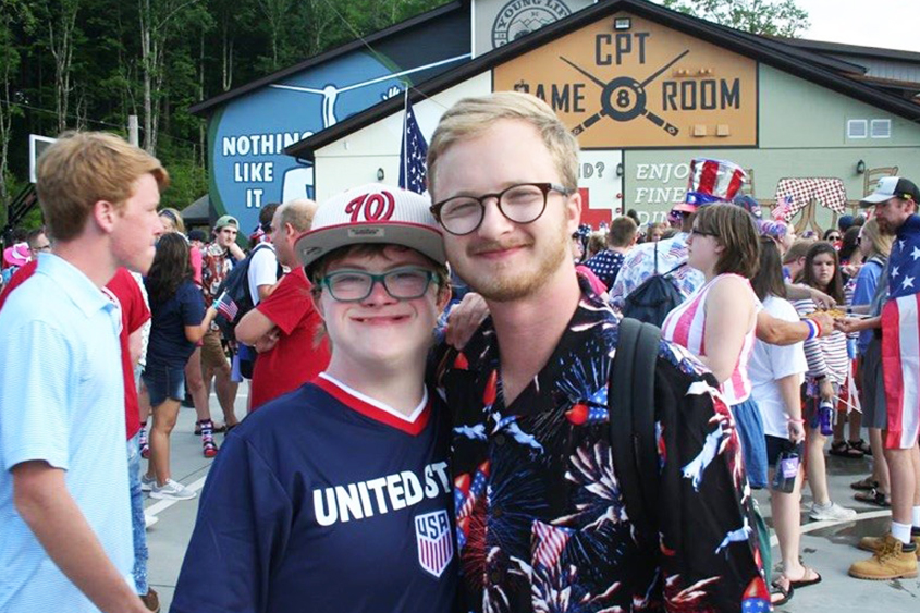 A man is standing with a special needs student. Both are smiling. 