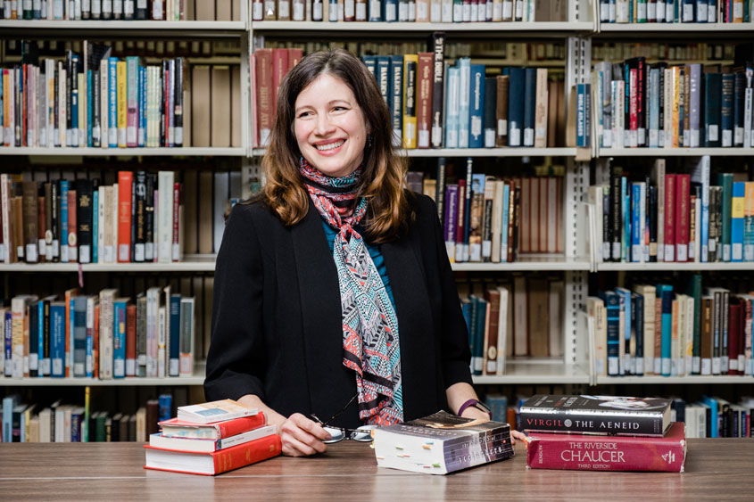 A women is standing with a few books. 