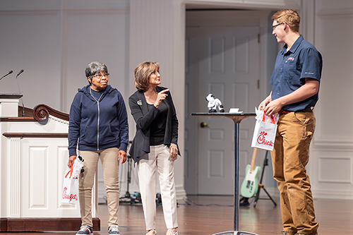 students holding Chick-fil-A while interacting on stage with Trudy Cathy White