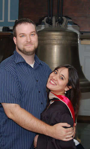 Jessica with her husband James standing in front of the bell