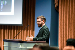 picture of a man in a business suit speaking at a podium in front of people