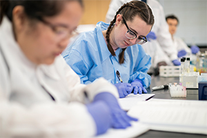 student writing in a lab journal surrounded by test tubes