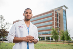 man standing infornt of hospital building wearing white DBU lab coat 