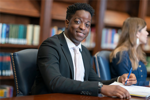 male student in a suit writing in journal while smiling