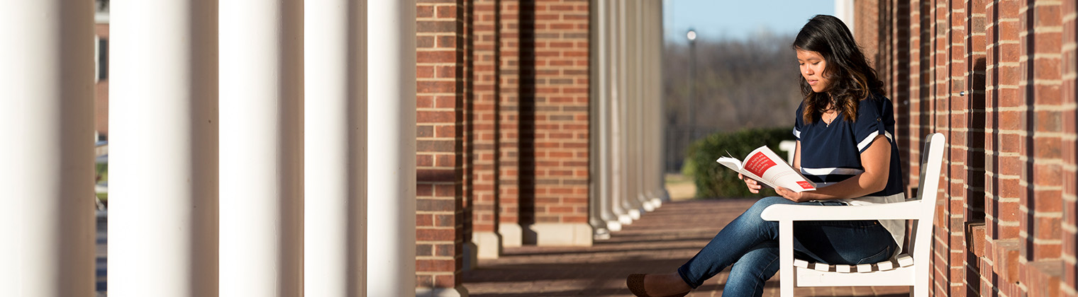 DBU college student reading on campus outside