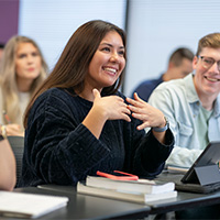 student smiling and talking in a classroom with students seated behind her